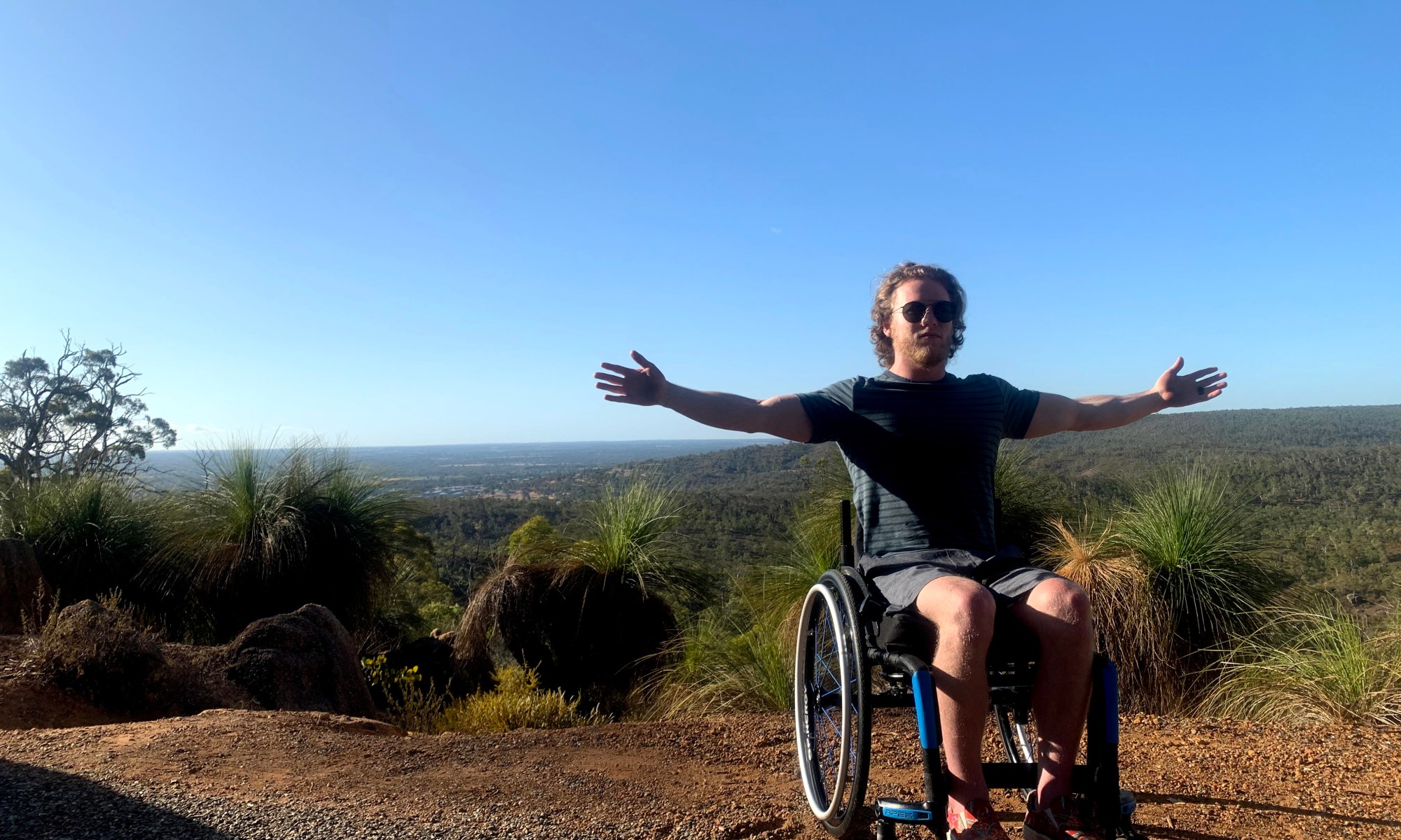 Cosmo wearing sunglasses with his arms spread like Tony Stark from Iron Man 1 with Australian views in the background
